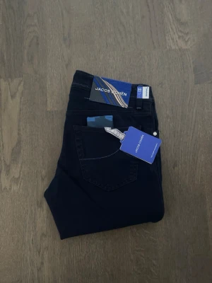 Mörkblå jeans från Jacob Cohën, stl 30 - Helt nya Jacob Cohen-jeans i populära modellen Nick. Tillverkade i exklusiv denim med perfekt passform och hög komfort. Klassisk mörk färg som fungerar lika bra till vardag som till finare tillfällen. Självklart med alla originaletiketter kvar. Ett självklart val för dig som uppskattar kvalitet och italienskt hantverk. Hör av dig för fler bilder/information
