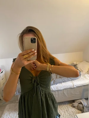 Grön linnetopp med knyt från 157 - Supersöt grön linnetopp från 157 i storlek XS. Toppen har v-ringning, knyt framtill och är ärmlös med volangdetaljer vid axlarna. Materialet är strukturerat och ger en avslappnad känsla. Perfekt för varma dagar och enkel att styla med jeans eller kjol.