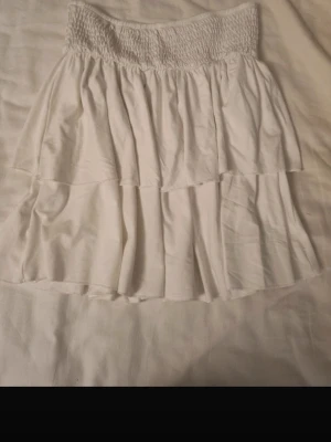 Vit volangkjol  - Säljer en vit kortkjol med bred smock i midjan och dubbla volanger. Fin volangkjol är xs men den har resår i midjan så passar säker s/m också 