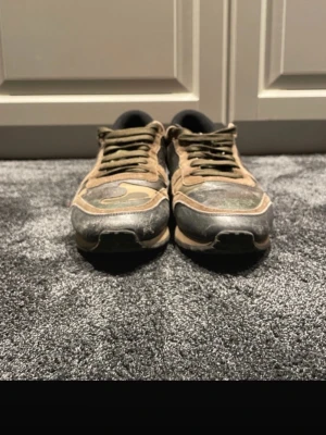 Valentino Rockrunner sneakers camo - Säljer ett par Valentino Rockrunner sneakers i camo-mönster med inslag av beige, grön, svart och en röd detalj på hälen. Skorna har snörning, platt sula och coola nitar på baksidan. Materialmix av mocka och skinn för en lyxig känsla. Självklart äkta ✅ Ställ så mycket frågor ni vill 🌟