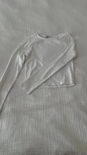 Vit långärmad croppad topp Stradivarius - Säljer en stilren vit långärmad topp från Stradivarius i storlek S. Toppen är croppad med rund hals och har en enkel, clean look. Materialet är mjukt och stretchigt, perfekt för att matcha med jeans eller kjol.