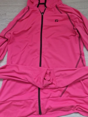 Rosa zip-hoodie från Röhnisch - Säljer en snygg rosa hoodie från Röhnisch med hel dragkedja och huva. Tröjan har svarta detaljer längs sömmarna och loggan på bröstet. Perfekt för träning eller chill, tillverkad i mjukt syntetmaterial som känns skönt mot huden. Priset kan diksuteras