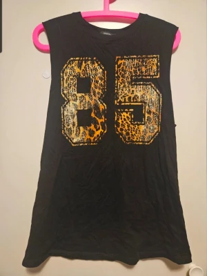 Sportigt linne med leopardtryck – Forever 21, strl S - Coolt och bekvämt linne från Forever 21 med stort "85"-tryck i glittrigt leopardmönster. Perfekt för sommaren eller ett avslappnat vardagslook! Svart basfärg med snyggt tryck i guld/leopard.  Välanvänd inga hål eller fläckar dock en lös tråd vid ena ärmen.    