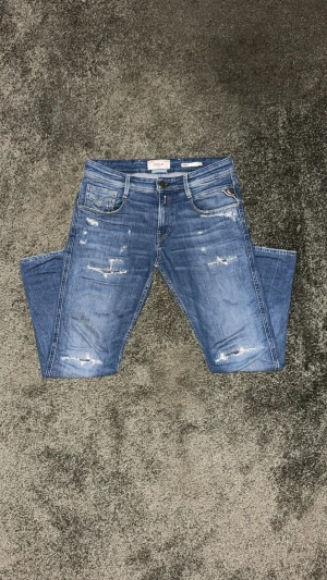 Replay Anbass blå jeans med slitningar - Snygga blå Replay Anbass jeans med slitna detaljer och klassisk femficksdesign. Jeansen har en slim fit passform och är tillverkade i mjukt denim med coola slitningar på framsidan. Perfekt för dig som gillar en elegant grish stil. Har du frågor är det bara att skicka! Priset är inte hugget i sten – kom med ett rimligt bud.