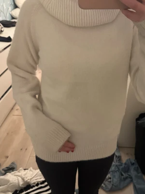 Vit polotröja med bred krage - Säljer en vit polotröja med bred, ribbad krage och långa ärmar. Tröjan har en mjuk och stickad känsla med ribbade muddar vid ärmslut och nederkant. Perfekt för kyliga dagar och enkel att matcha med jeans eller leggings.