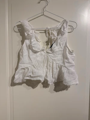 Vit topp med volanger  - Toppen har volanger och knyte i ryggen, supersöt till sommaren!