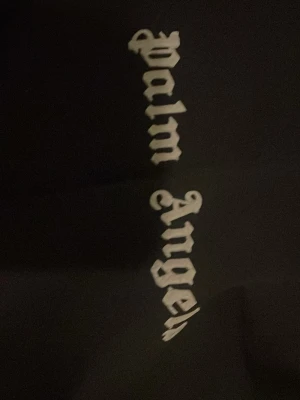 Svart Palm Angels t-shirt med tryck - Svart t-shirt från Palm Angels med ikoniskt vitt tryck i gotisk stil på bröstet. Klassisk passform och rund hals. Materialet är mjukt och känns skönt mot huden, perfekt för dig som gillar streetwear och vill sticka ut med en snygg logga.