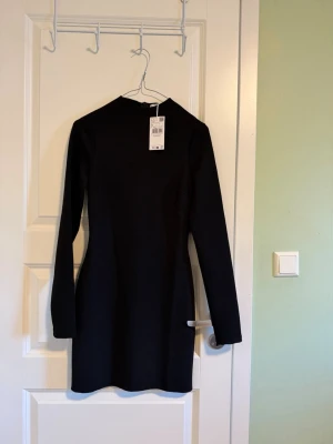 Svart långärmad kortklänning - Säljer en stilren svart klänning från Mango med lång ärm och enkel, figurnära passform. Klänningen är kort och har en rund halsringning, perfekt för dig som gillar minimalistisk stil.