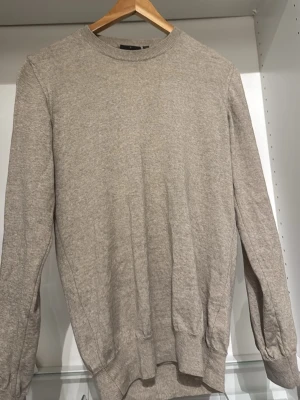  Tröja Oscar Jacobson - Snygg beige stickad tröja från Oscar Jacobson i storlek S. Tröjan har rund hals, ribbade muddar och är långärmad. Perfekt för dig som gillar stilrena och klassiska plagg med skön passform. Tillverkad i Italien och passar bra till både jeans och chinos.