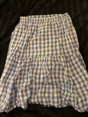 Blårutig långkjol från Monki - Säljer en blåvit långkjol från Monki i storlek L. Kjolen har ett rutigt mönster och är gjord i mjuk bomull. Den har en volangdetalj och har en normal passform. Perfekt för dig som gillar en somrig stil. Använd max en gång 🩷