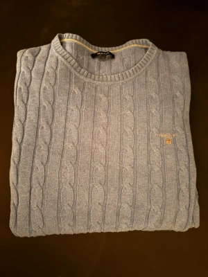 Ljusblå stickad tröja från GANT - Snygg ljusblå stickad tröja från GANT med klassiskt kabelstickat mönster och rund hals. Tröjan har lång ärm och ribbade muddar vid ärmslut och nederkant. GANT-logga broderad på bröstet för en clean och stilren look. Pris kan diskuteras.