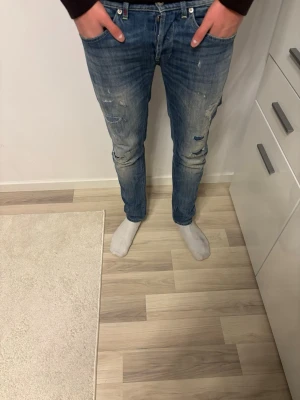 Dondup George jeans med slitningar - Säljer ett par blå jeans från Dondup  med coola slitningar och detaljer på benen. Modellen har normal passform och klassisk femficksdesign. Jeansen är tillverkade i jeansmaterial och har en snygg tvättad look med distressed effekter.