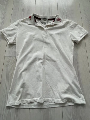 Gucci pikétröja  - Säljer en riktigt snygg vit Gucci pikétröja med broderade detaljer på kragen, bland annat en röd orm och en fackla. Kragen har även klassiska Gucci-ränder i grönt och rött. Storlek S! Ej använd. Vid intresse bara att höra av sig! 