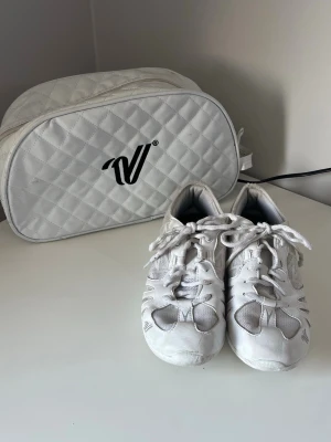 Vita Cheerleading skor från varsity med väska - Vita cheearleading skor i EUR storlek 39. Dom är lite slitna i tån och hälen på ena skon men de är inget som stör ens träning eller skulle inte trigga skavsår. I övrigt är dom i bra skick men man ser att dom är använda. Man får också en Väsk till skorna.
