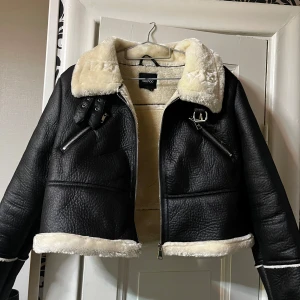 Svart teddyjacka från Boohoo - Säljer en svart teddyjacka från Boohoo med krämvit päls på krage, insida och detaljer. Jackan har dragkedjor framtill, två fickor med dragkedja och snygga spännen vid kragen. Mysig för kallare dagar 