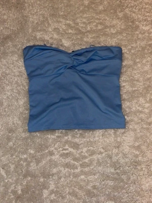 Blå bandeau tubtopp med smock stl M - Säljer en blå bandeau tubtopp från Bikbok i stl M med snygg twistad detalj framtill och smockad baksida för extra komfort. Toppen är axelbandslös,Perfekt för varma dagar och enkel att matcha med jeans eller kjol. har bara legat i garderoben så aldrig använd, köparen betalar frakt☺️