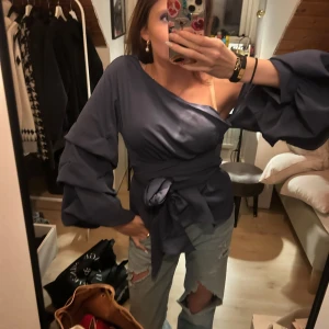 Mörkblå offshoulder blus med volangärm - Snygg mörkblå blus med offshoulder-design och långa volangärmar. Blusen har ett knytband i midjan som ger en fin siluett och extra stilpoäng. Jätte fin , classy topp med fina volanger . Perfekt till vardags och på fest. Använd fåtal, max 3 gånger  Nypris 400kr! öppen för sänkning