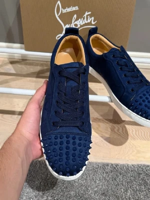 Mörkblå mocka sneakers Christian Louboutin - Säljer ett par mörkblå sneakers från Christian Louboutin i mjuk mocka med vita sulor. Skorna har coola nitar på tån, rund tå och klassisk snörning. Insidan är beige och märkt med Louboutin Paris. Perfekta för dig som vill sticka ut!