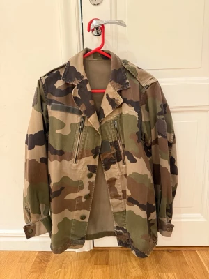 Grön kamouflagefärgad jacka - En militärinspirerad cool jacka i kamouflagemönster med en amerikansk flagga på ryggen. Jackan har inga lappar, jag uppskattar den till storlek M💗