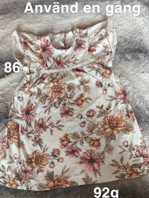 Blommig kortklänning från Newbie - Supersöt kortklänning från Newbie med blommigt mönster. Klänningen har volangdetaljer vid axlarna och är ärmlös. Perfekt för varma dagar och somriga vibes!🌸 Använd en gång. Storlek 86