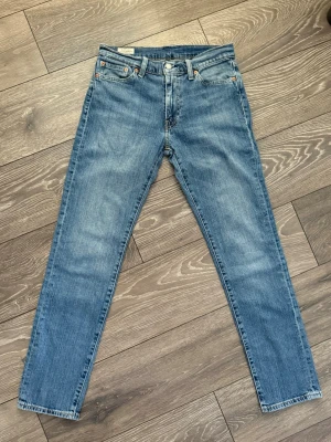 Levi's 511 blå jeans W30 L32 - Säljer ett par klassiska Levi's 511 jeans i blå tvätt. Modellen har normal passform med raka ben och fem fickor. Jeansen är tillverkade i slitstarkt bomullsmaterial och har den ikoniska läderpatchen bak i midjan samt röda Levi's-taggen på bakfickan.
