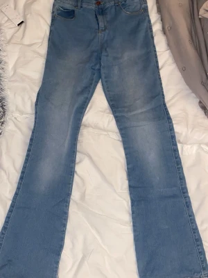 Bootcut ljusblå jeans - Säljer ett par ljusblå bootcut jeans med klassisk femficksdesign och knappgylf. Jeansen har en snygg utsvängd passform från knät och är tillverkade i mjukt denimtyg. 