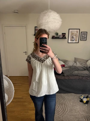 vit blus - Secondhand - Superfin och luftig vit blus med vackert mörkbrunt/svart broderi runt halsringningen och ärmarna. Blusen har en smickrande V-ringning och en lös, bekväm passform. Perfekt för sommarens fester, semestern eller till ett par snygga denim-shorts. Ett måste för dig som gillar den bohemiska stilen! • Stil: Boho / Folkloristisk • Storlek: Uppskattas till S/M (se bild för passform) • Skick: Fint begagnat skick.