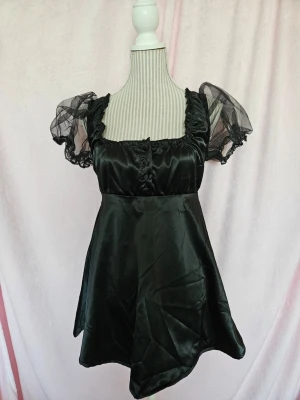 Svart klänning från Lazy Oaf  - Svart klänning med puffärmar i mesh. Klänningen har en fyrkantig halsringning och knappar framtill. Det finns en broderad detalj baktill med texten "Pretty Ugly". Använd en gång, mycket fint skick. Köpt för ca 1400 kr med frakt och importmoms inräknat men är slutsåld . Har sytt upp den lite. Storlek 8. 