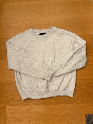 Ljusgrå sweatshirt från Lager 157, XS - En enkel och stilren ljusgrå sweatshirt från Lager 157 i storlek XS. Tröjan har rund hals, långa ärmar och ribbade muddar vid ärmslut och nederkant. Mjuk insida i fleece som gör den extra skön att ha på sig. Perfekt för chill eller skola. 99% Bomull, 1% Viskos.