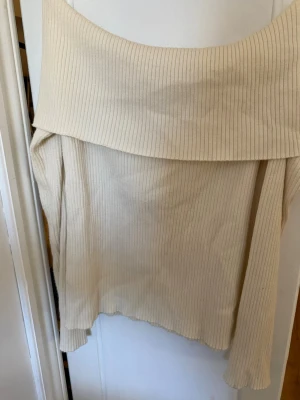 Offsholder topp - Säljer en ribbad offshoulder topp i beige med lång ärm. Är i storlek L men passar även M och S på grund av det stretchiga tyget. Har använts varsamt med inga tecken på användning. Säljer på grund av att den inte kommer till användning längre. Skriv för frågor och gärna innan du trycker på köp💞