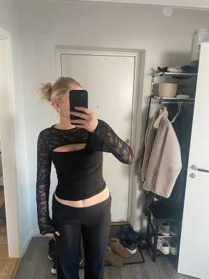 Svart spetsblus från Gina Tricot - Supersnygg svart blus från Gina Tricot med långa ärmar i genomskinlig spets och en cool cut out-detalj vid bröstet. Toppen är figurnära och har en blandning av slät och spetsig textur som ger en trendig look.