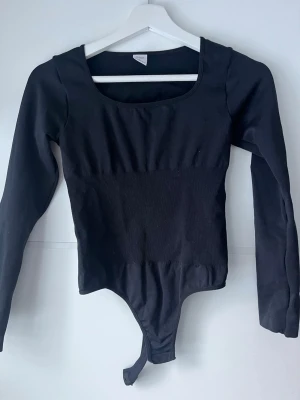 Svart långärmad body - Säljer en svart långärmad bodysuit med rund halsringning. Toppen är tight i modellen och har knäppning nedtill. Perfekt att styla med jeans eller kjol för en clean look.