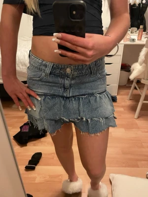 Jeanskjol med volanger från Gina Tricot - Supersöt kort jeanskjol från Gina Tricot i blå denim med två lager volanger och råa kanter.Perfekt för dig som vill ha en trendig och söt sommar kjol. Storlek 152 och men passar nog storleken över och under. Säljer pågrund av att den blivit för liten i midjan💓