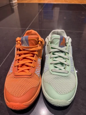 Nike JA1 mismatched sneakers i mintgrön och orange - Unika Nike sneakers med en sko i mintgrönt och en i orange. Båda har mesh-ovandel, snörning och mönstrade detaljer i ljusblått och grått. Snyggt mönster på sidorna och yttersulan, samt rund tå och platt sula. Perfekt för dig som vill sticka ut med färg och stil.