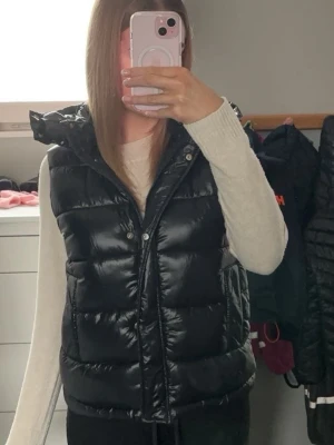 Svart dunväst med huva monki - Säljer en svart, glansig dunväst med huva och dragkedja plus knappar framtill, från monki. Den är aldrig använd och köpte för 399💕 Huvan går att ta bort (knappar) ifall man föredrar det