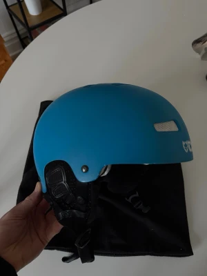 Blå TSG skidhjälm - Säljer en blå TSG skidhjälm med flera ventilationshål och justerbart hakband. Hjälmen har vit TSG-logga och passar perfekt för vintersport. Utsidan är i hård plast och insidan är vadderad för extra komfort. Celsius skidglasögonen ingår ej. L/XL