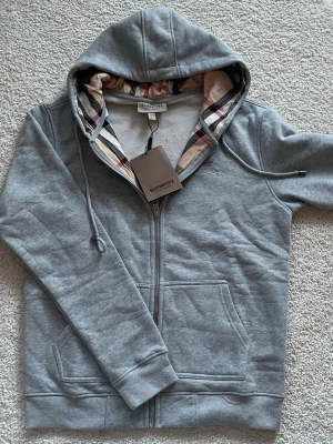 Burbery hoodie grå - Fett grå hoodie från Burbery i storlek L men passar även M. Hoodien är aldrig använd! Det är bara att fråga om ni undrar nåt eller vi se fler bilder