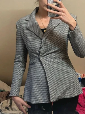 Rutig kavaj med markerad midja - Säljer en snygg rutig kavaj med markerad midja och klassisk krage. Jackan har lång ärm och stängs framtill med dold knäppning. Perfekt för dig som vill ha en stilren och trendig look.