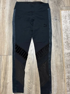 Svarta leggings från Puma med sammet - Snygga svarta leggings från Puma med bred midja och sammetspaneler längs sidorna. Byxorna har coola meshdetaljer och ett diskret Puma-logo broderat på låret. Perfekta för träning eller chill, med skön stretch och tight passform. Obs mindre i storlek, skulle säga passar S 