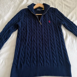 Marinblå kabelstickad tröja Polo Ralph Lauren - Säljer en helt ny och oanvänd kabelstickad tröja från Polo Ralph Lauren. Den här tröjan är i en djup marinblå färg och är perfekt för höst- och vintersäsongen. Den är tillverkad i högkvalitativt material och är otroligt mjuk och bekväm att bära.