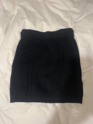 Svart stickad kortkjol Gina Tricot - Supersnygg svart stickad kortkjol från Gina Tricot i storlek XS. Kjolen har bred resår i midjan och diskreta kabelstickade detaljer framtill. Perfekt att styla med en oversized tröja eller boots för en trendig look.