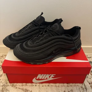 Nike Air Max 97 Svarta sneakers - Nike Air Max 97 sneakers i helsvart med vågiga linjer och reflekterande detaljer. Perfekta för dig som gillar streetstyle och sportig vibe. Passar bra till kalla säsonger. Slitage ses endast på yttersulan.