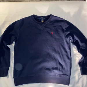 Mörkblå sweatshirt från Polo Ralph Lauren - Klassisk mörkblå sweatshirt från Polo Ralph Lauren med rund halsringning och röd broderad logga på bröstet. Tröjan har långa ärmar och ribbade muddar vid ärmslut och nederkant. Perfekt för en stilren och avslappnad look. storlek 14-16 år (xs), bra skick inga synliga defekter. Hör gärna av er vid frågor!!