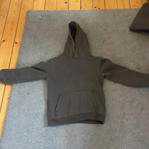 Mörkgrå hoodie från H&M - Säljer en enkel och stilren mörkgrå hoodie från H&M i storlek 146/152. Tröjan har huva, långärmade ärmar och en stor magficka framtill. Perfekt för chill dagar och passar till det mesta. Materialet är mjuk bomullsmix som är skön mot huden.