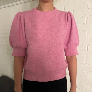 Rosa stickad tröja med puffärm - Superfin rosa stickad tröja med puffiga korta ärmar och ribbade muddar. Tröjan har en rund halsringning och är gjord i ett mjukt material som känns skönt mot huden. Perfekt för dig som gillar trendiga detaljer och vill ha en färgklick i garderoben.💞