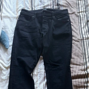 Svarta tapered jeans Jack & Jones - Svarta jeans från Jack & Jones i modellen Tapered/Mike. Klassisk femficksdesign, knappgylf och snyggt avsmalnande ben. Tillverkade i stretchig bomullsblandning för extra komfort. Perfekta för dig som gillar en modern och avslappnad look.