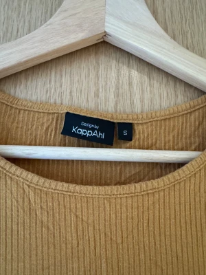 Senapsgul ribbad topp KappAhl - Senapsgul ribbad topp från KappAhl i storlek S. Modellen har puffiga korta ärmar och rund halsringning. Tillverkad i mjuk viskosmix med stretch för en skön passform. Perfekt för dig som gillar en enkel men trendig look. Kortärmad ribbad topp med puffärm i mjukt material. Gul / Orange. 