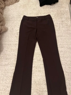Bruna kostymbyxor från Bik Bok - Snygga bruna kostymbyxor från Bik Bok i storlek 34. Byxorna har utsvängda ben, bälteshällor och fickor bak. Materialet är mjukt och har en stretch. de är helt oanvända och i nytt skick. 
