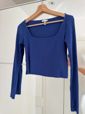 Blå ribbad tröja H&M - Säljer en kornblå croppad topp från H&M i storlek S. Toppen har lång ärm, fyrkantig ringning och är ribbad för en snygg struktur. Materialet är en mix av bomull, polyester och elastan vilket gör den stretchig och bekväm. Blå långärmad topp, ribbat tyg och lite kortare modell. Storlek XS-S. 