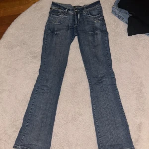 Blå bootcut jeans från Lome - Snygga blå jeans från Lome med bootcut passform och klassisk femficksdesign. Jeansen har ljusa slitningar, kontrastsömmar och dekorativa detaljer på bakfickorna. Tillverkade i mjukt denimtyg som sitter skönt hela dagen. Har sytt fast knappen då den fastnar pga den ramlade av ibland men det går bra inget man märker av under dagen! 